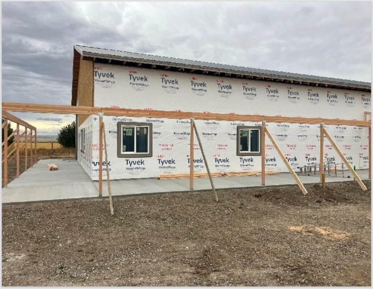 House under construction with Tyvek house wrap covering the wooden frame and walls, showing windows and a wooden deck