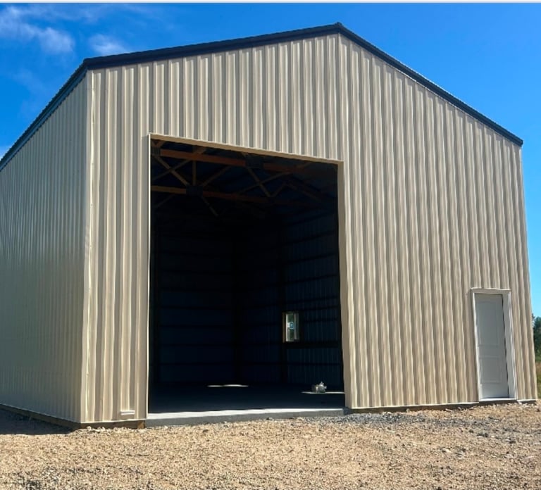 Metal agricultural storage building with large open bay door and corrugated steel walls against clear blue sky