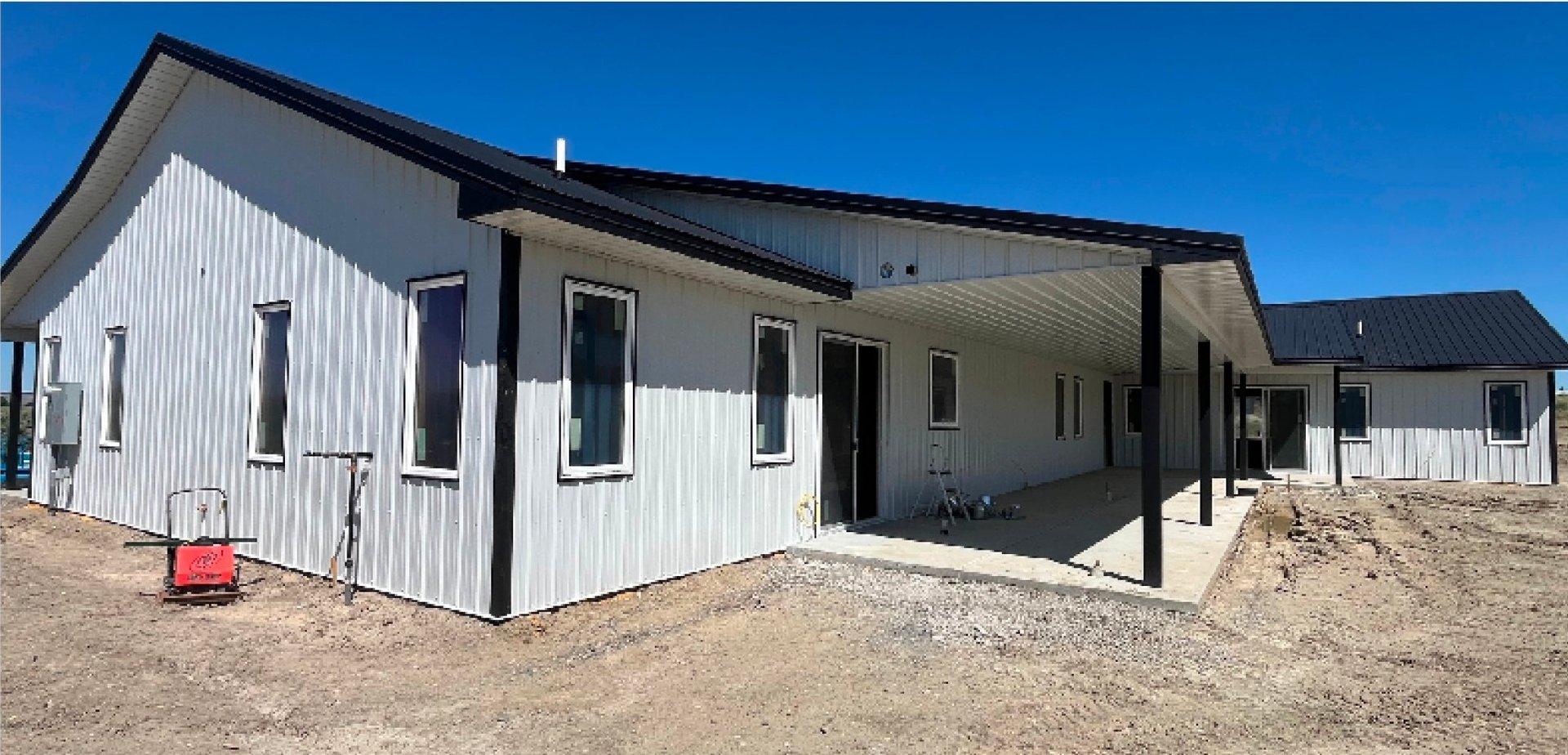 Modern modular house under construction with white metal siding and black trim against clear blue sky