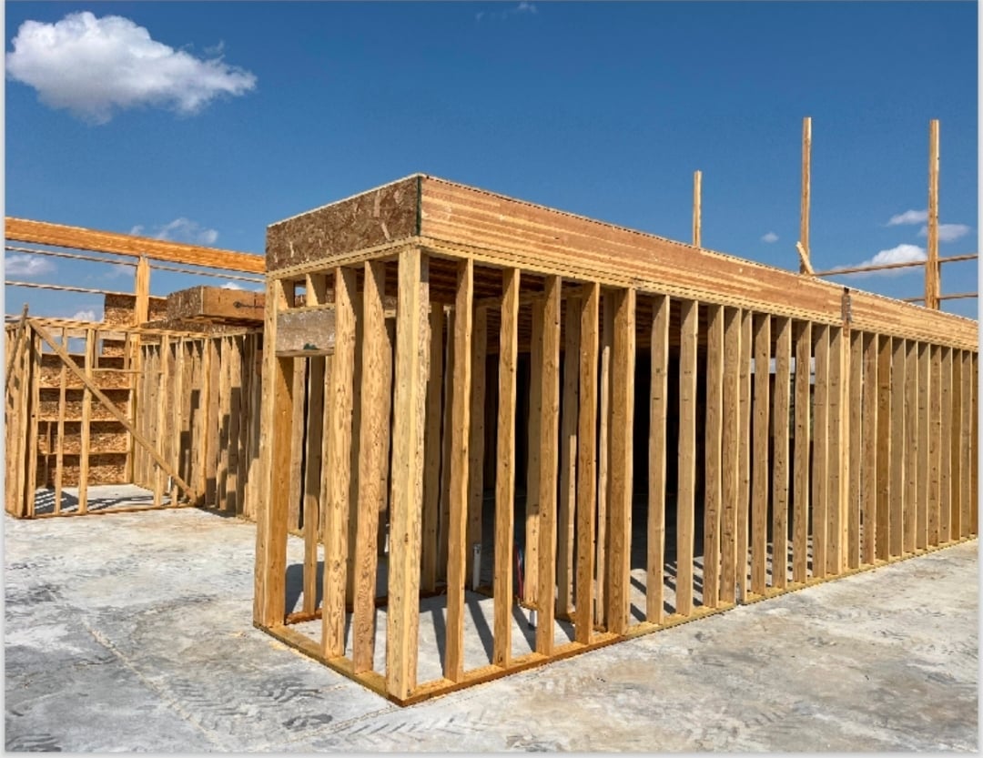 Wooden framed house structure under construction with exposed studs and roof beams against blue sky
