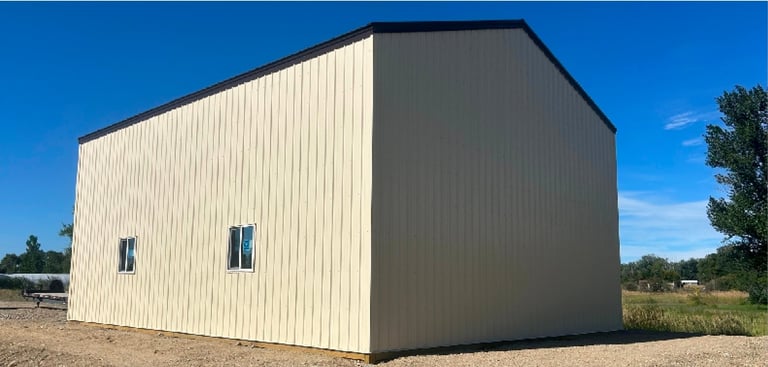 Modern rectangular metal shed with cream and dark gray corrugated siding, two small windows, situated on sandy ground under clear blue sky
